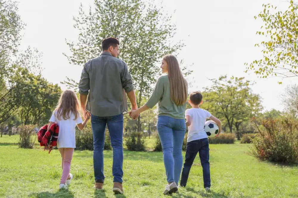 A family of four walking in a grassy park, holding hands and enjoying the outdoors.