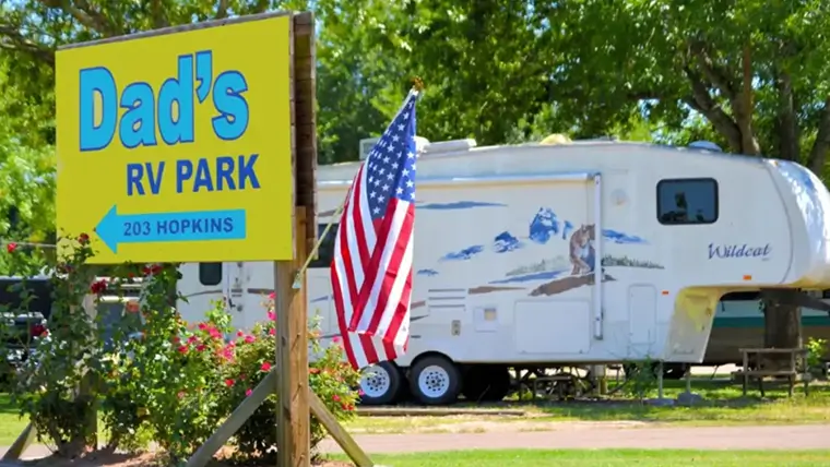Dad’s RV Park sign with American flag and RV campsite in the background